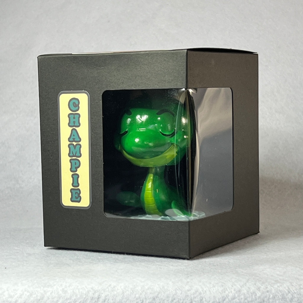 Green toy figure in a black box with 'Champie' label on a white background