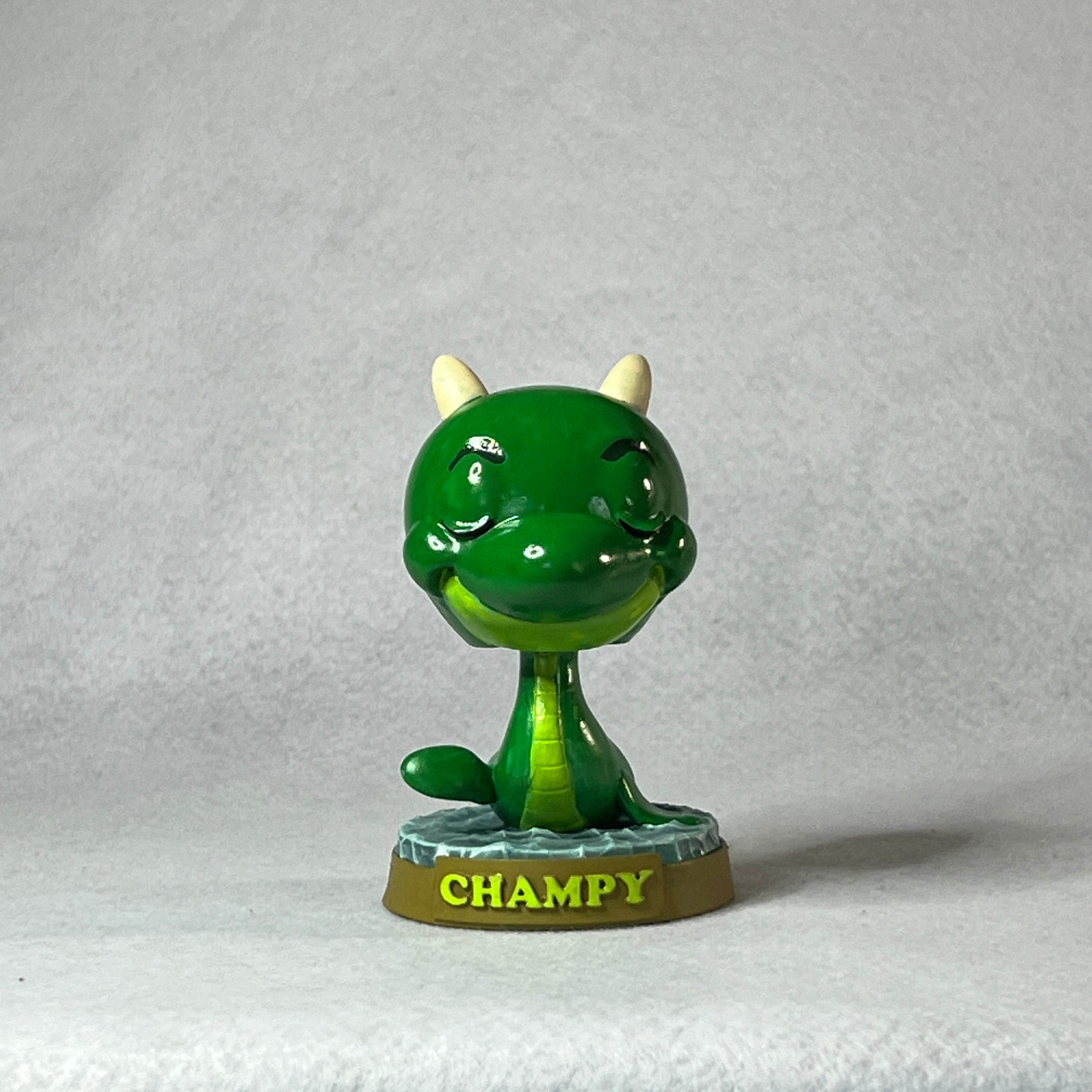 Green dragon-like figurine with 'Champy' on a gray background