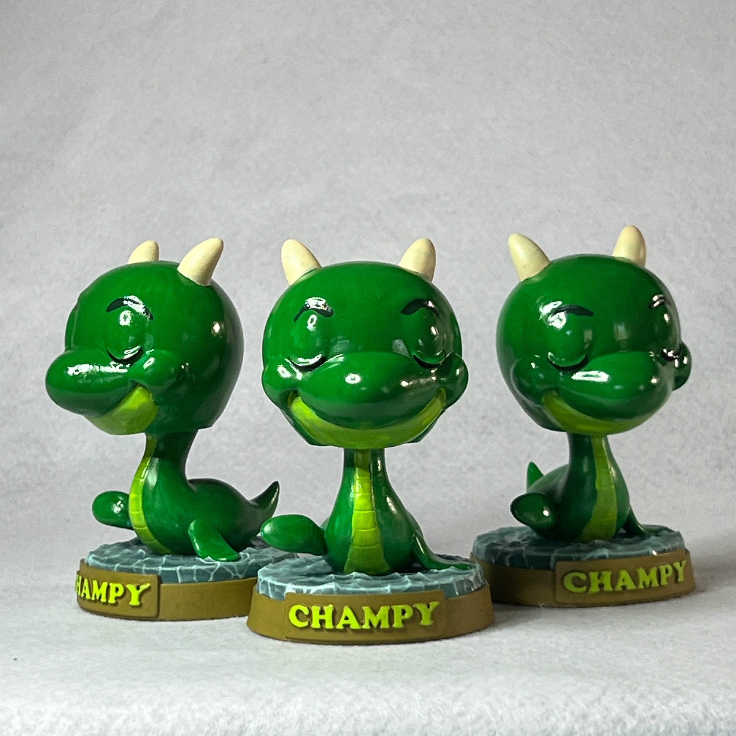 Three green dragon-like figurines with 'Champy' branding on a gray background