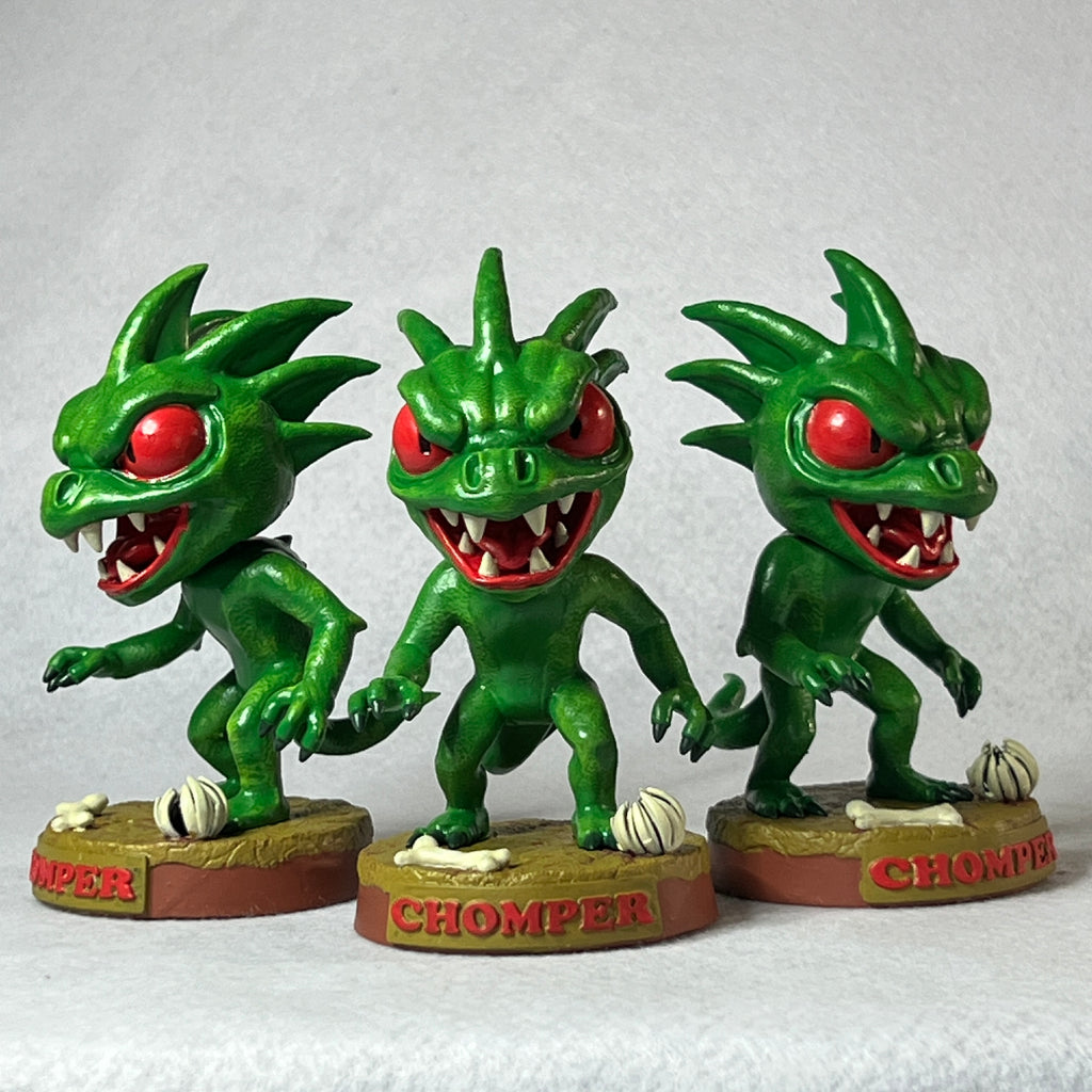 Three green dragon-like figurines with red eyes on a white background