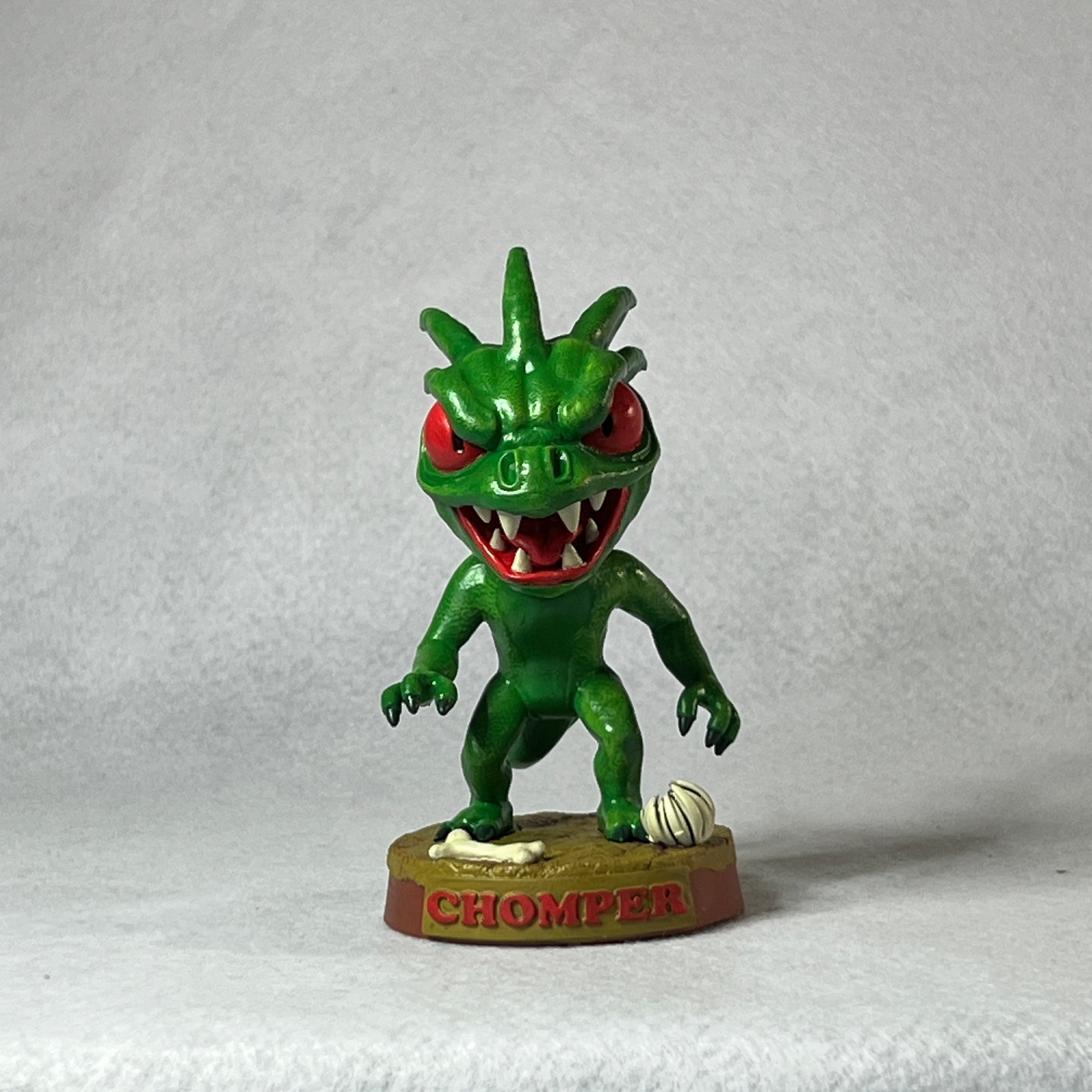 Green monster figurine with red eyes and open mouth on a white background