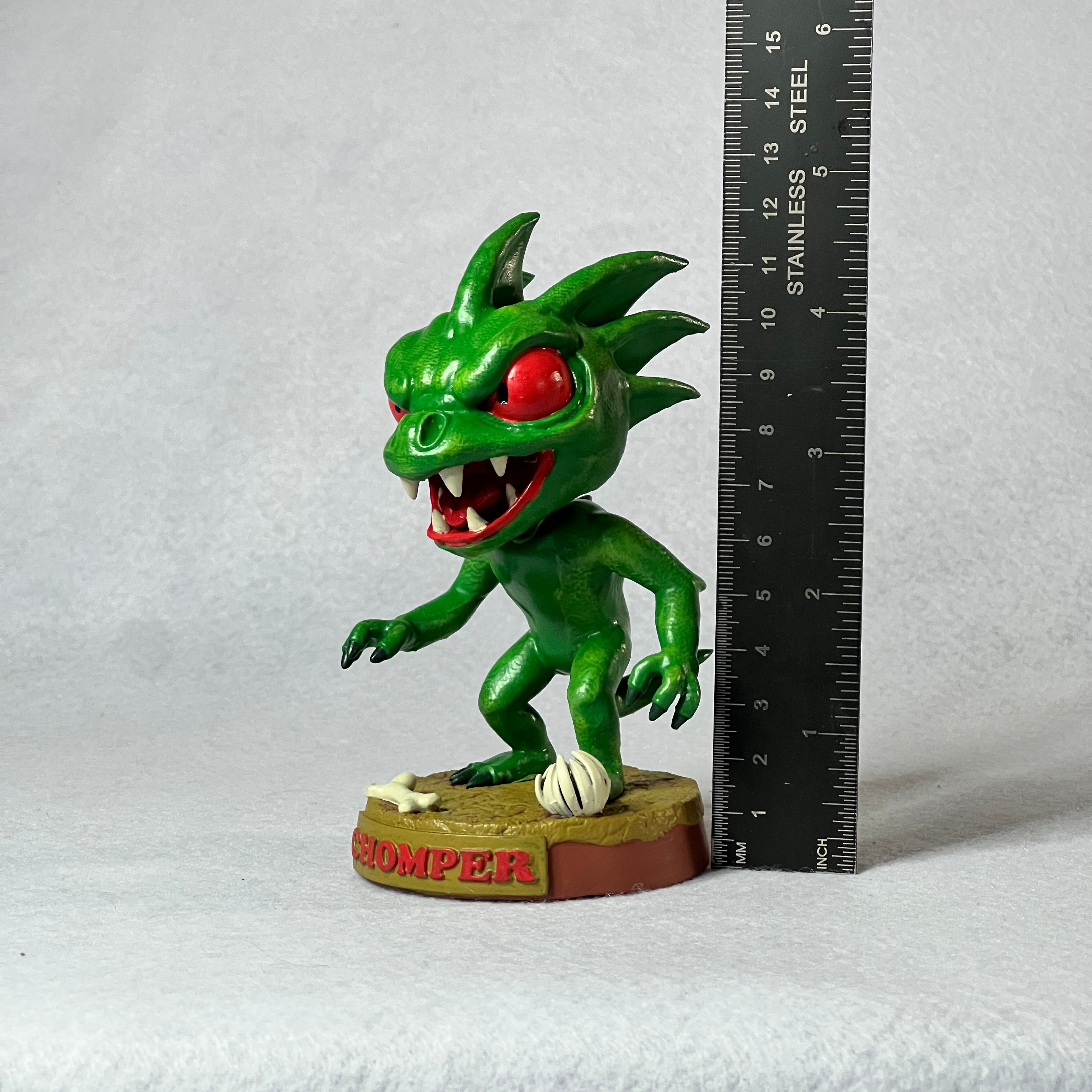 Green monster figurine next to a ruler on a white background