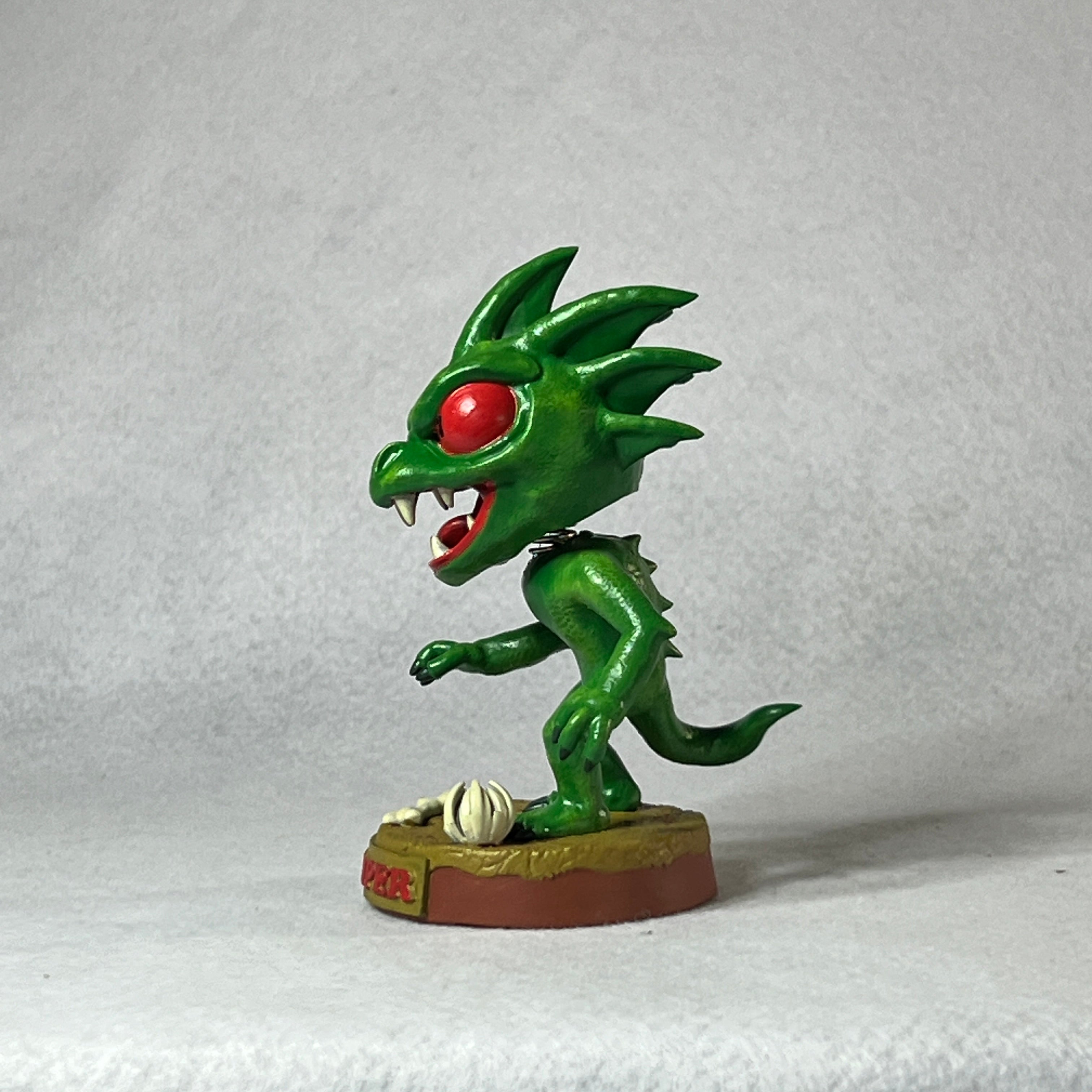 Green dragon-like figurine with red eyes on a white background
