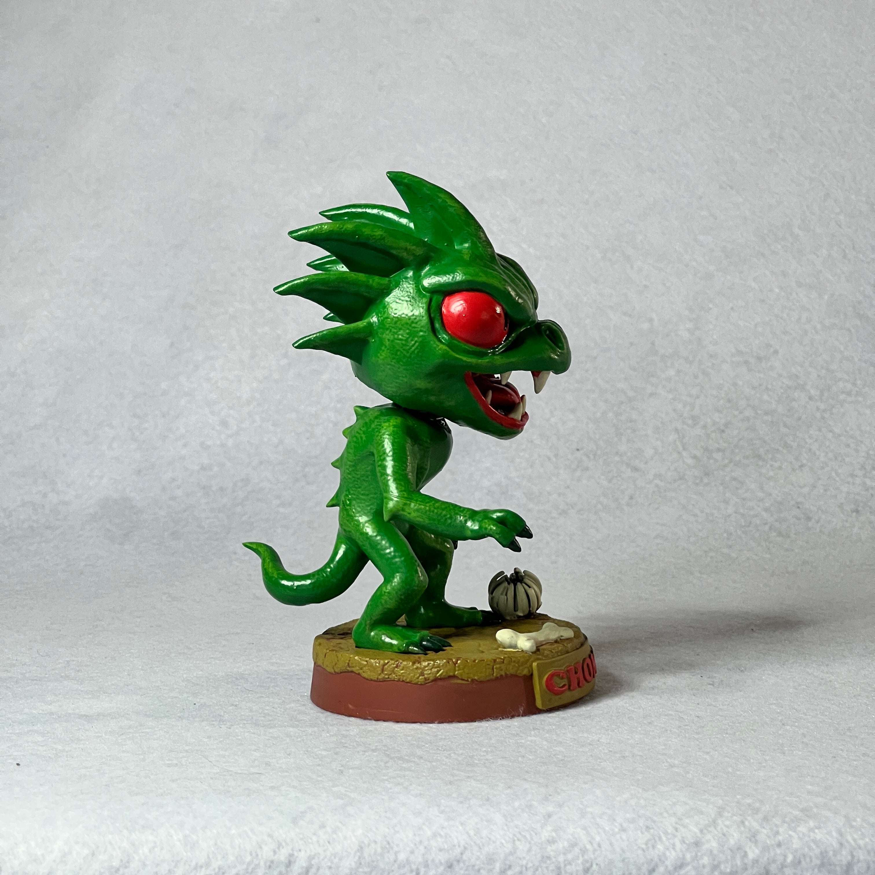 Green monster figurine with red eyes on a white background