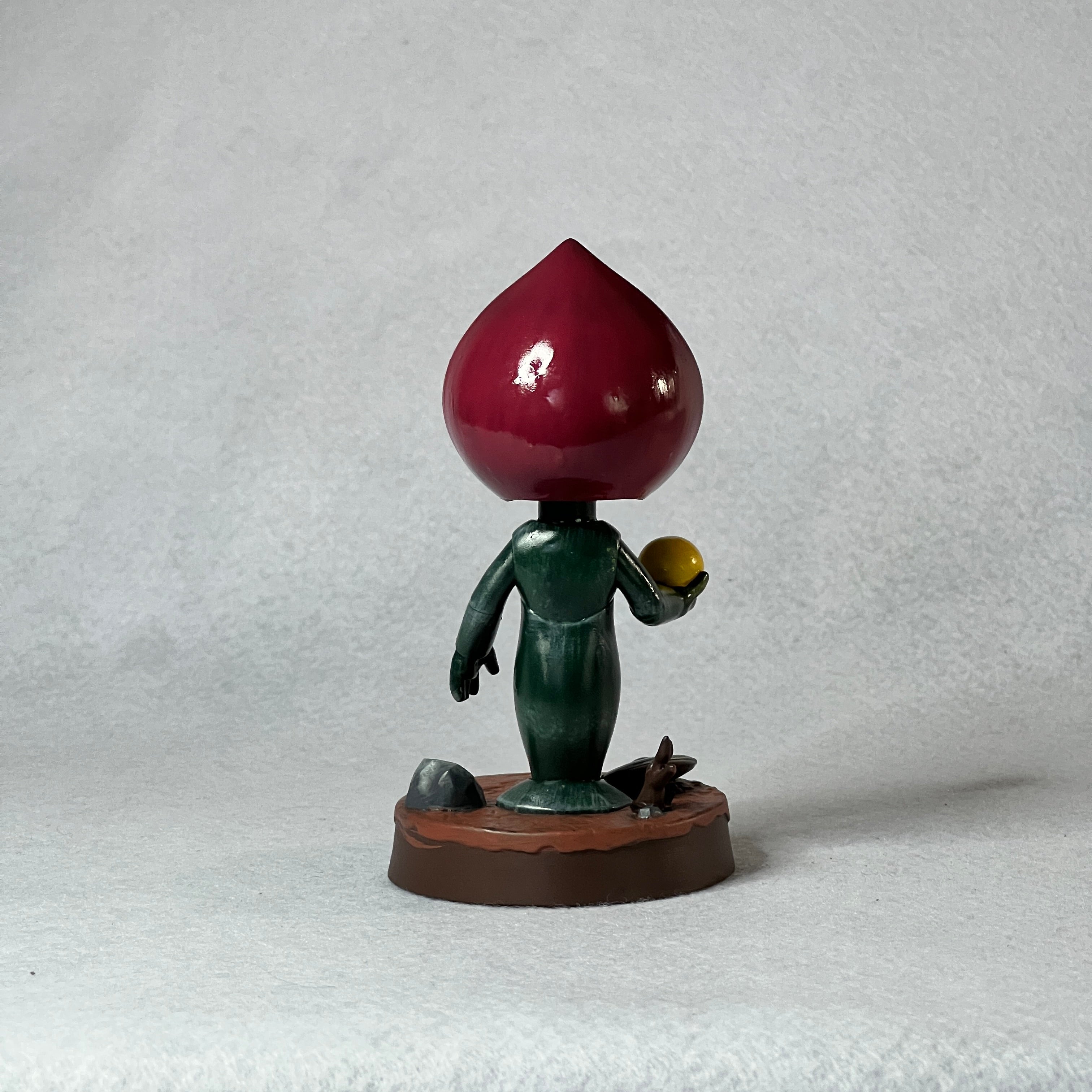Figurine with a large red teardrop-shaped head on a white background