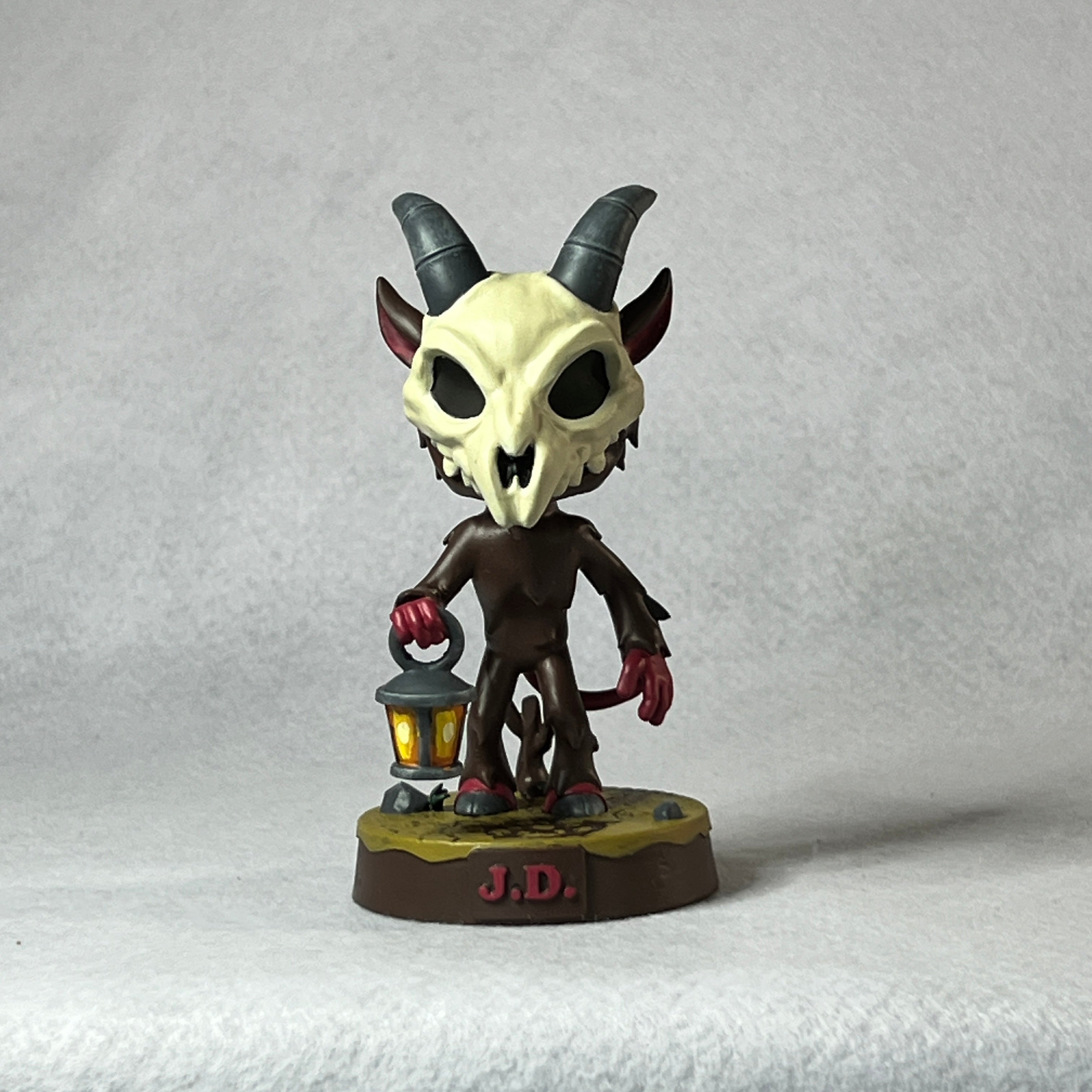 Figurine with skull-like face and horns holding a lantern on a textured gray background