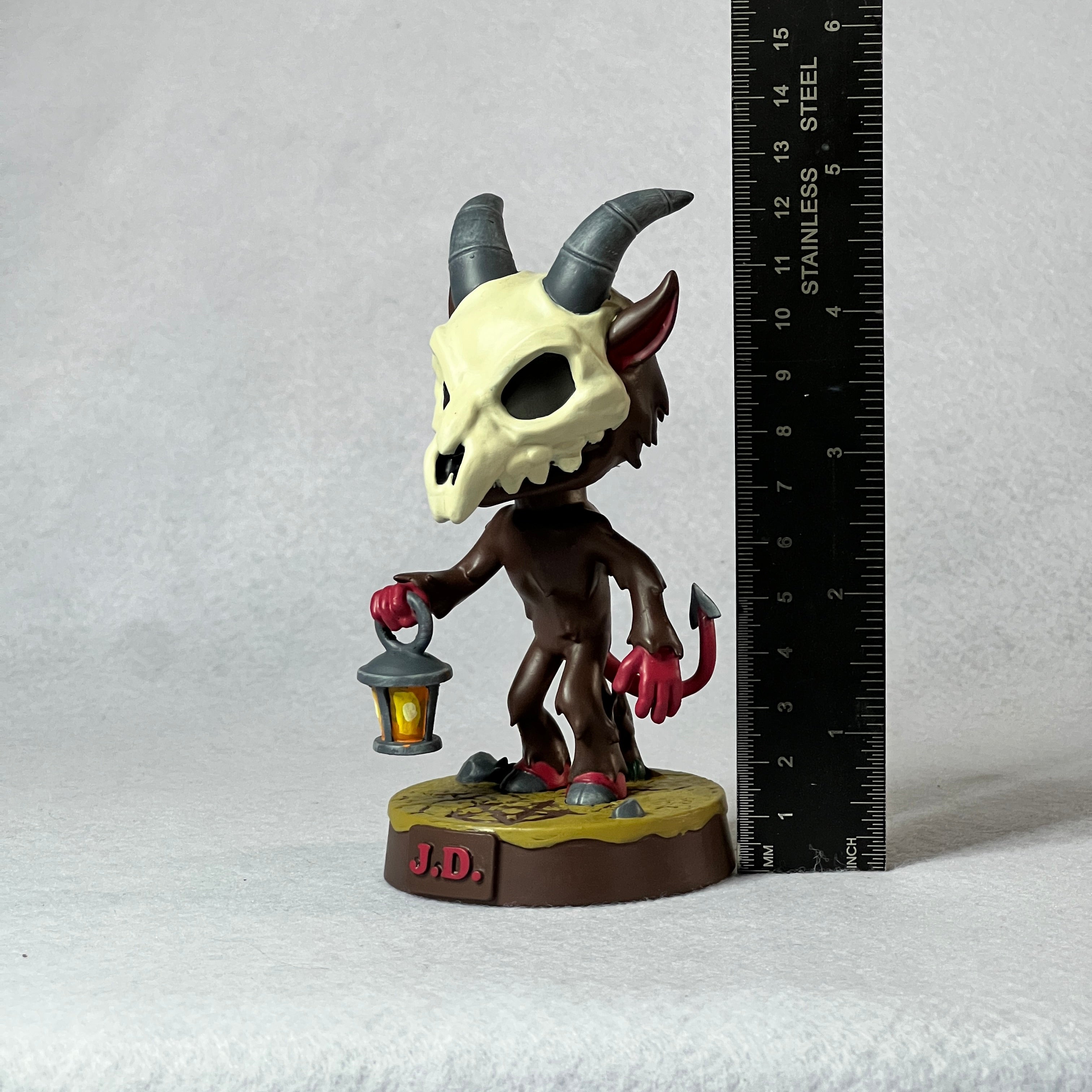 Devil figurine with a lantern next to a ruler on a white background