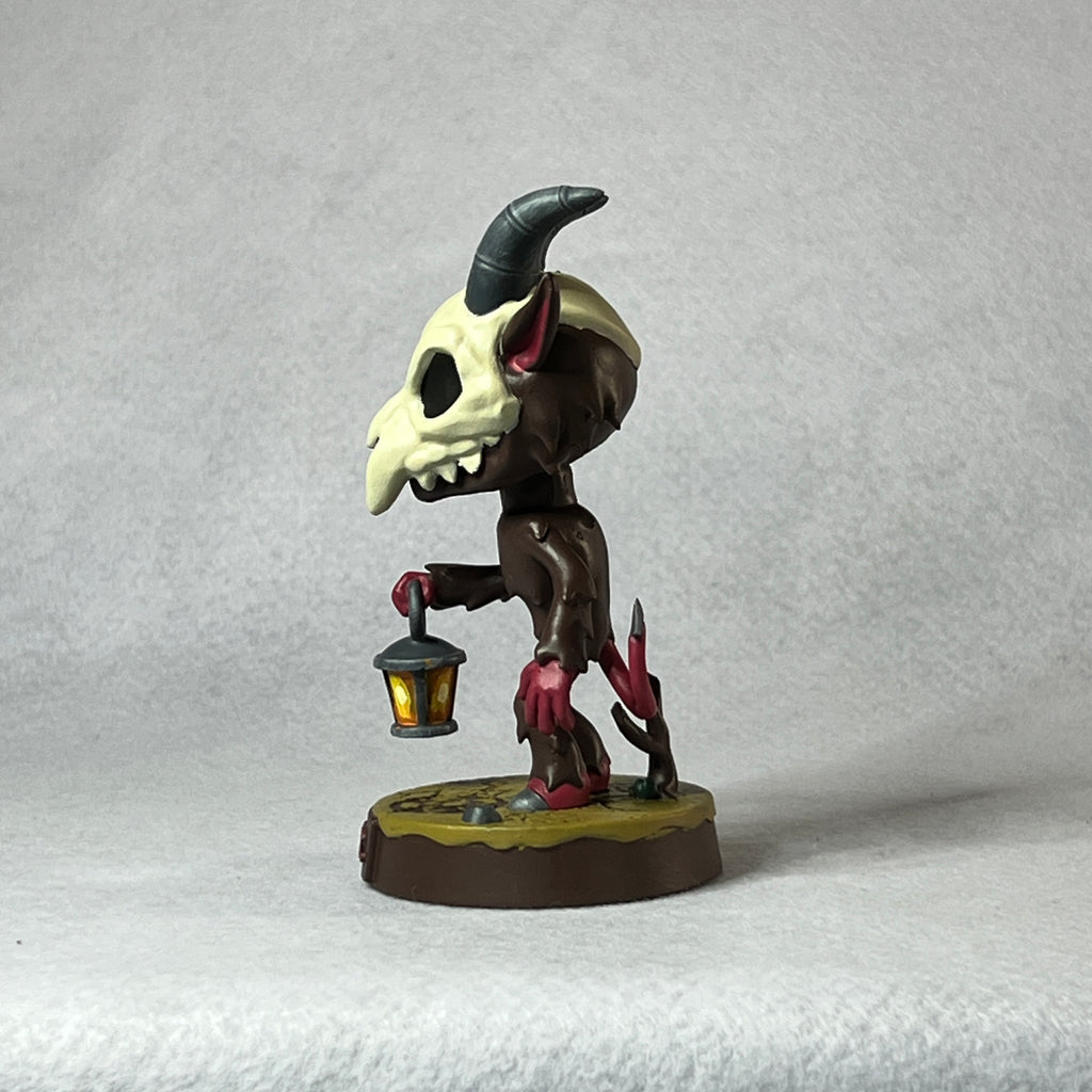 Small figurine with a skull-like head and lamp on a gray background