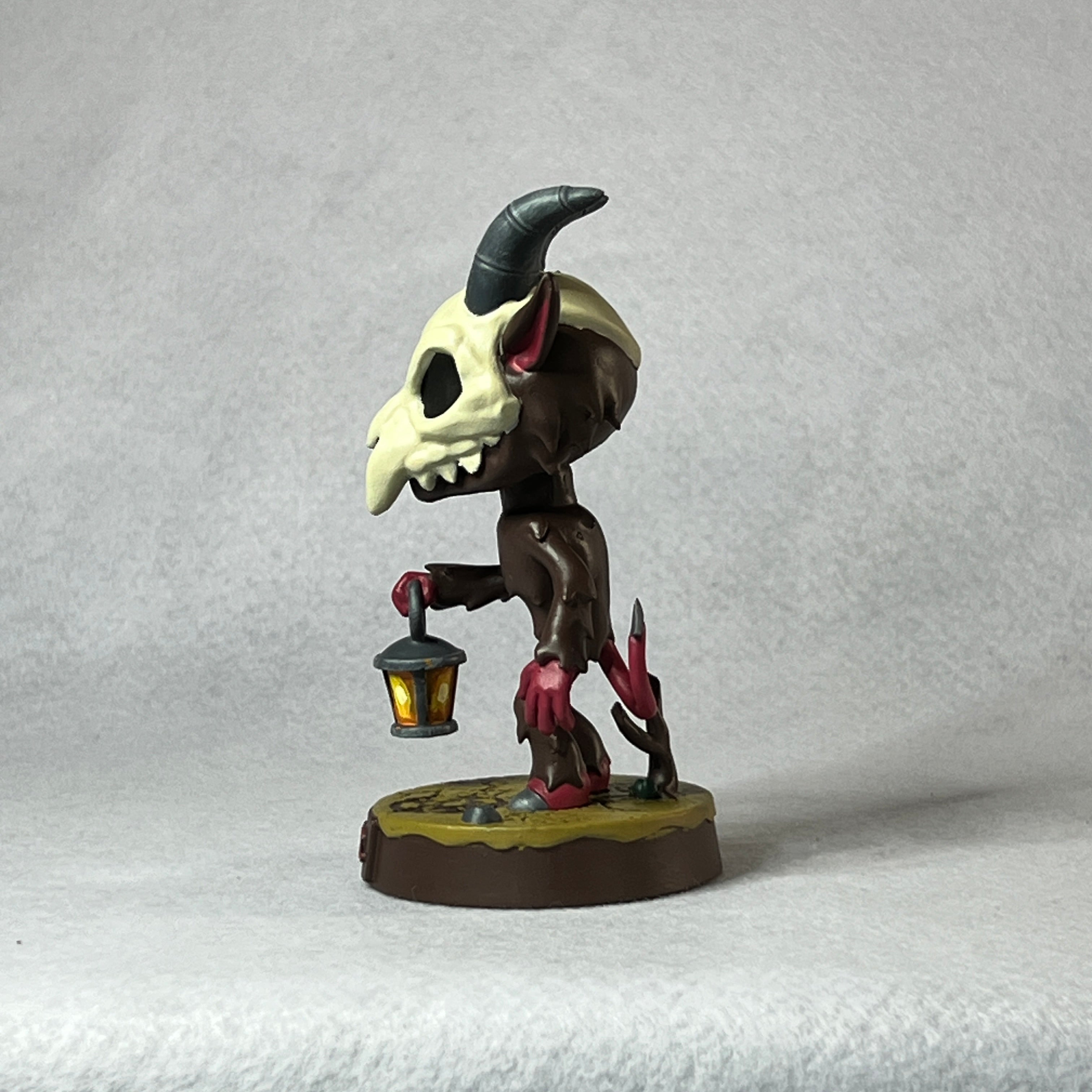 Small figurine with a skull-like head and lamp on a gray background