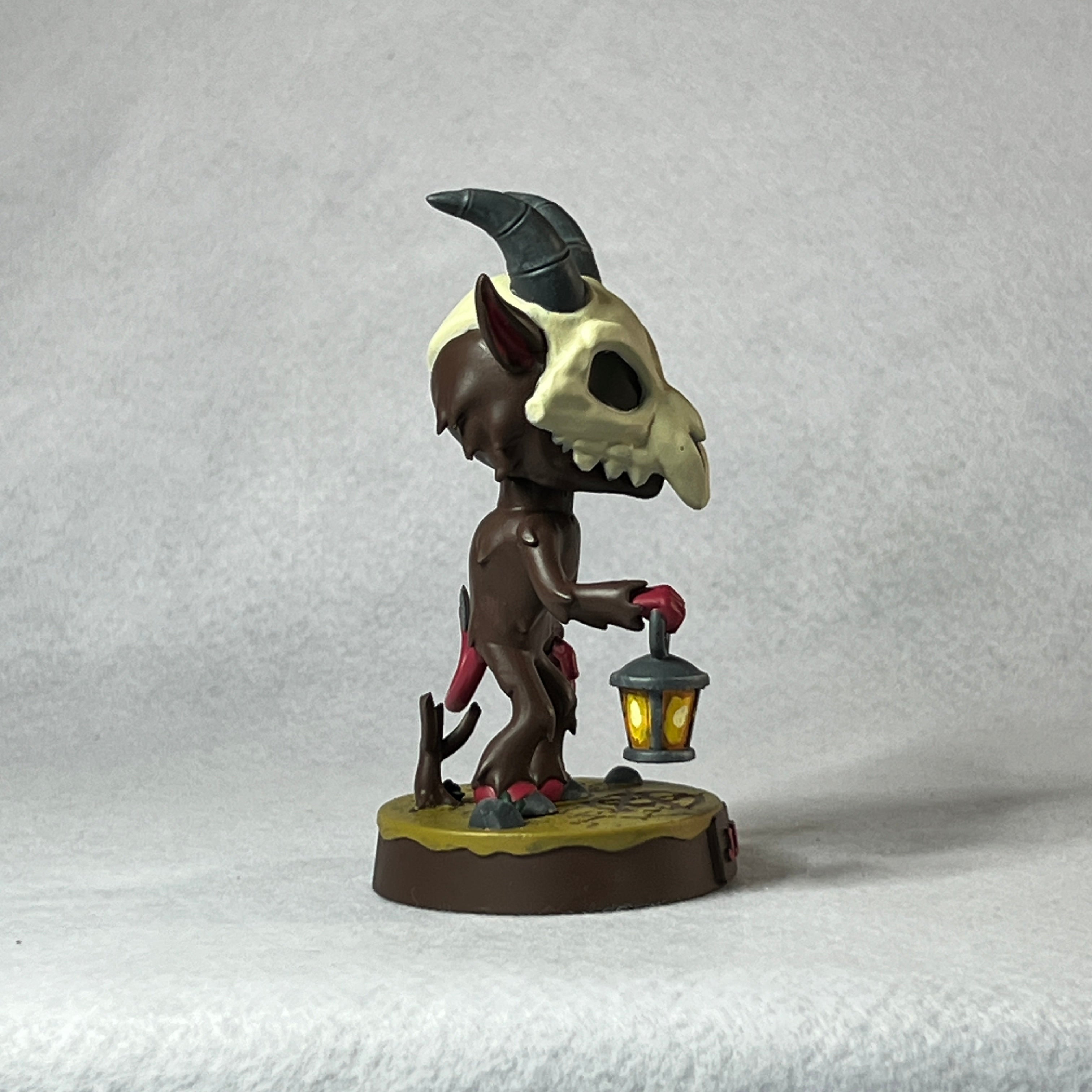 Figurine with a creature holding a skull and lantern on a textured gray background