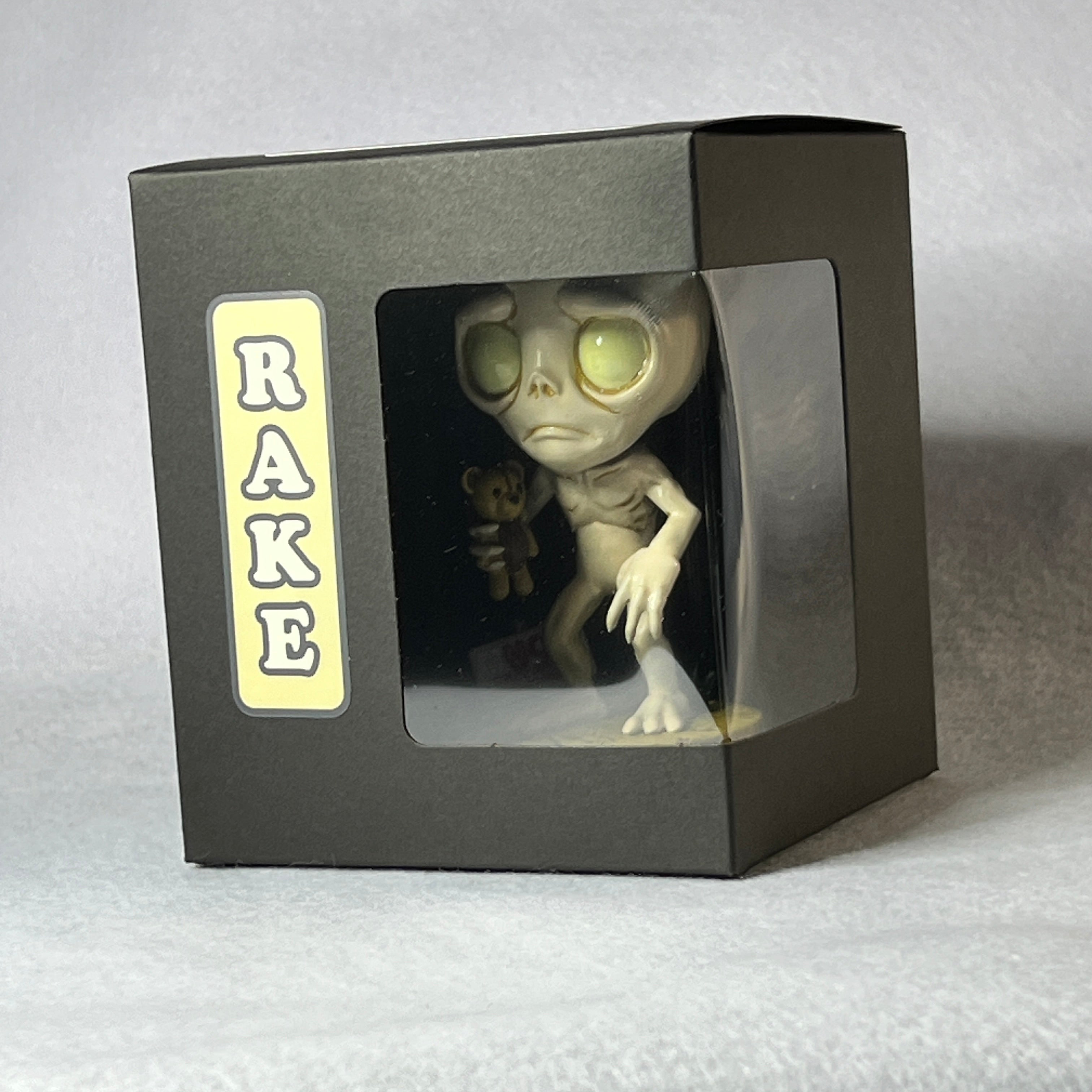 Alien figure in a box with 'RAKE' branding on a gray background